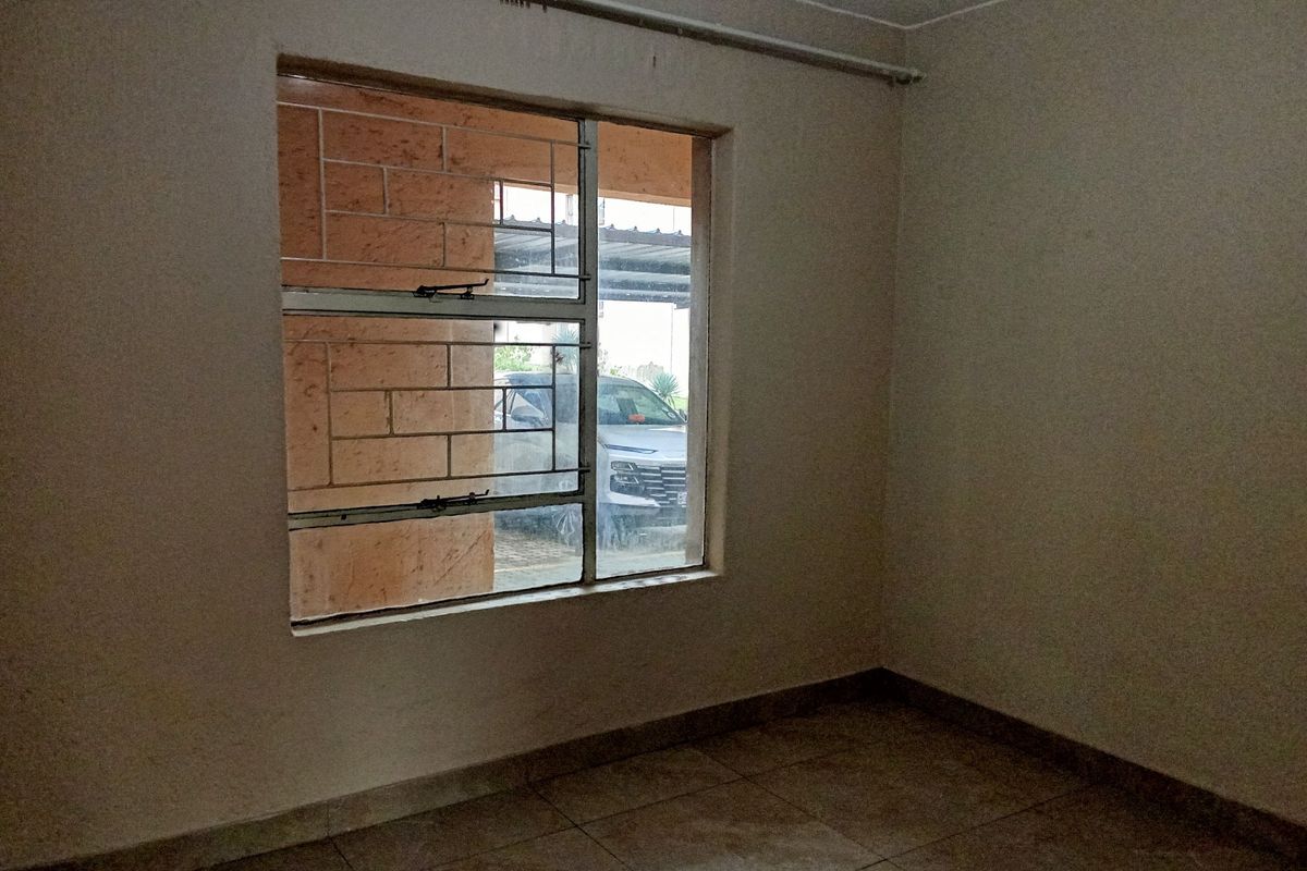 An empty bedroom featuring tiled flooring, a window with security bars, and a curtain rail, ready for personalization.