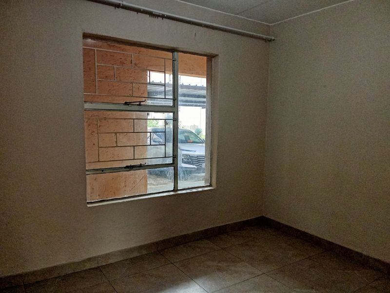 An empty bedroom featuring tiled flooring, a window with security bars, and a curtain rail, ready for personalization.