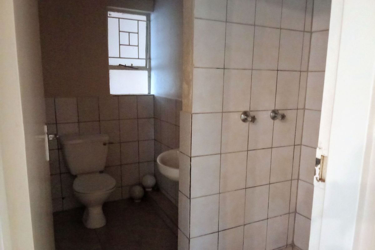 A functional bathroom featuring a shower, toilet, and basin with tiled finishes, requiring cosmetic updates to improve its overall condition and aesthetic appeal.
