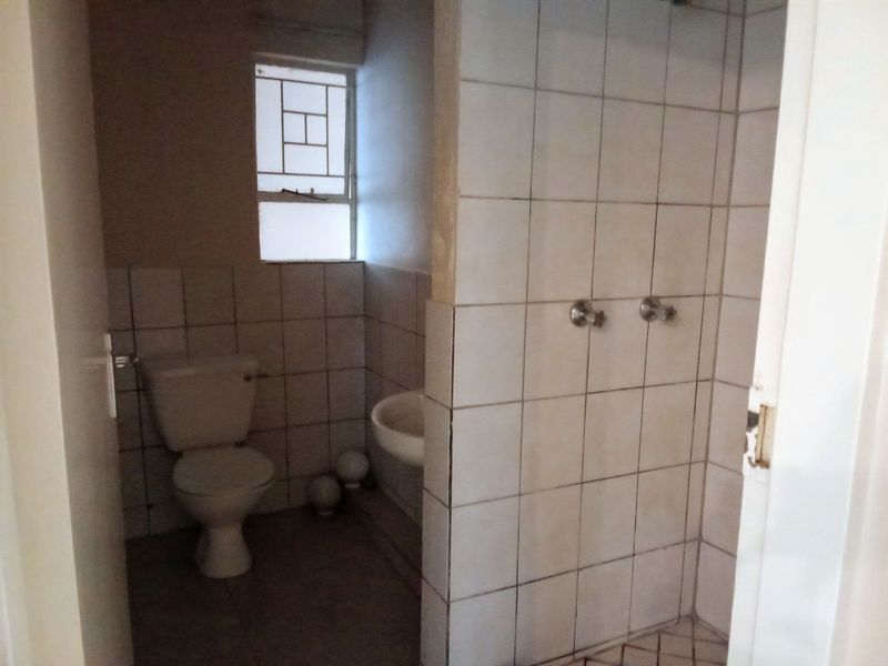 A functional bathroom featuring a shower, toilet, and basin with tiled finishes, requiring cosmetic updates to improve its overall condition and aesthetic appeal.