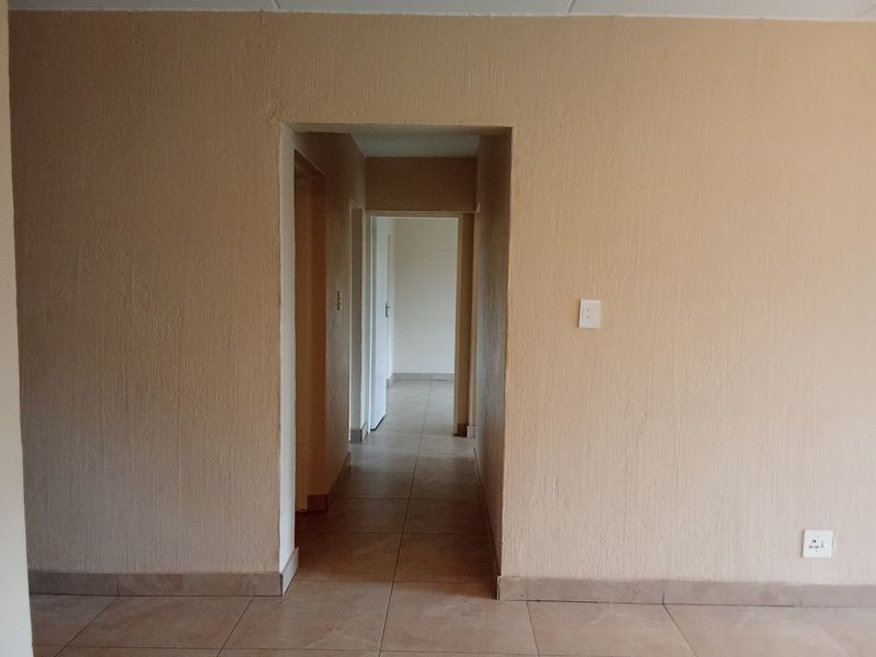 A vacant hallway featuring neutral textured walls and tiled flooring, providing access to adjacent rooms within the townhouse.