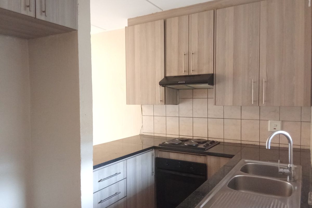 A functional kitchen featuring light wood-tone cabinetry, dark granite countertops, a built-in oven with hob, and a double bowl sink with tiled backsplash.