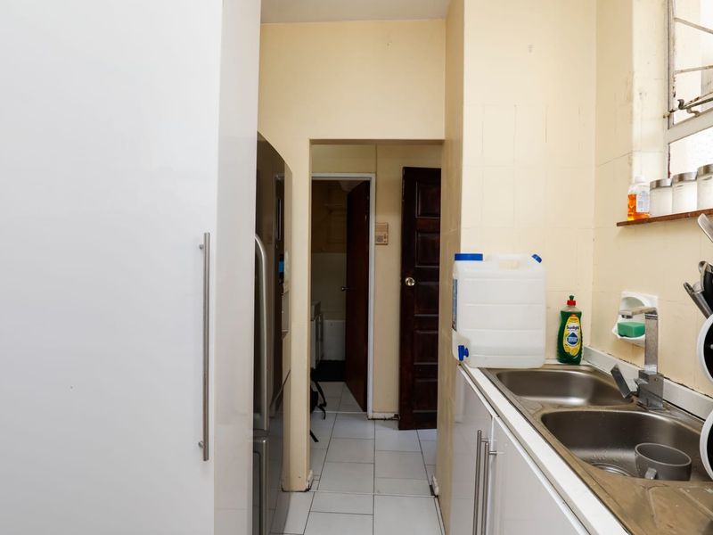 A functional kitchen area featuring a double stainless steel sink, tiled flooring, and tiled splashbacks, providing a practical layout for daily use.