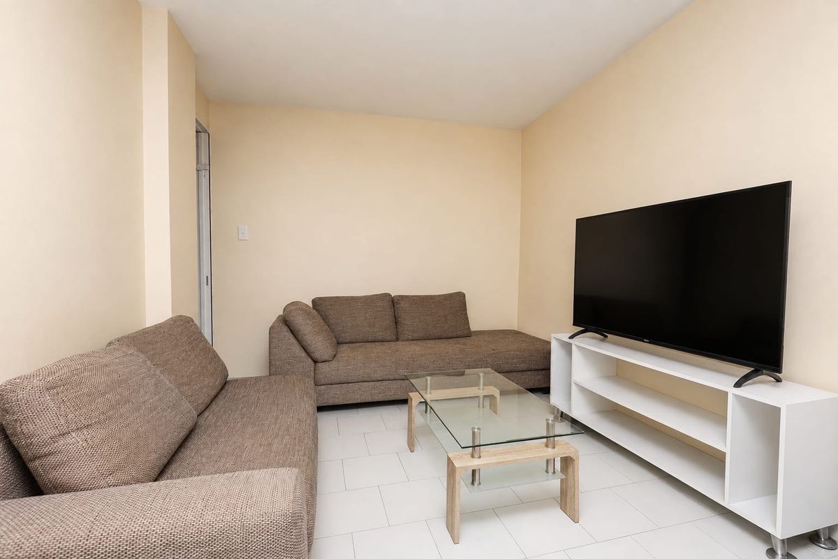 A simple living room featuring neutral wall paint and clean tiled flooring, providing a functional and well-lit space for relaxation.