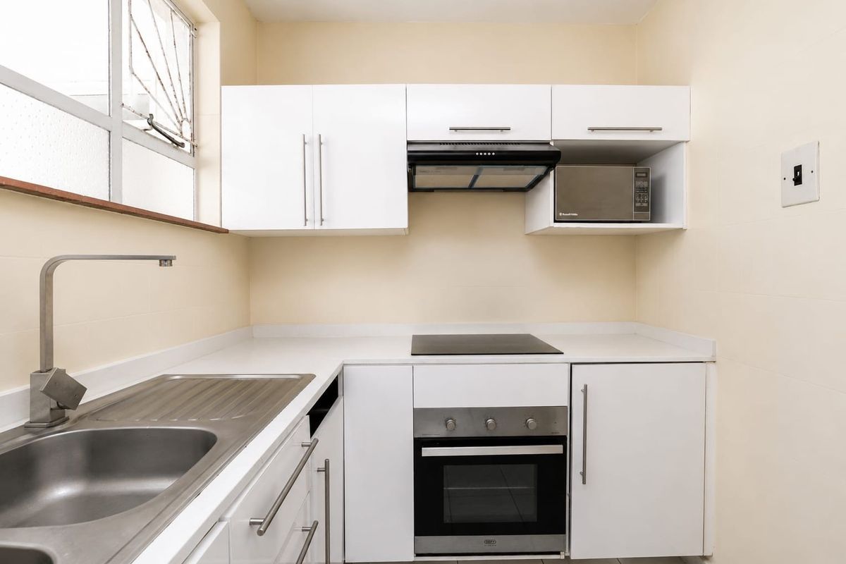 A clean, modern kitchen featuring white cabinetry, a stainless steel sink, built-in oven, electric hob, and an integrated extractor fan.