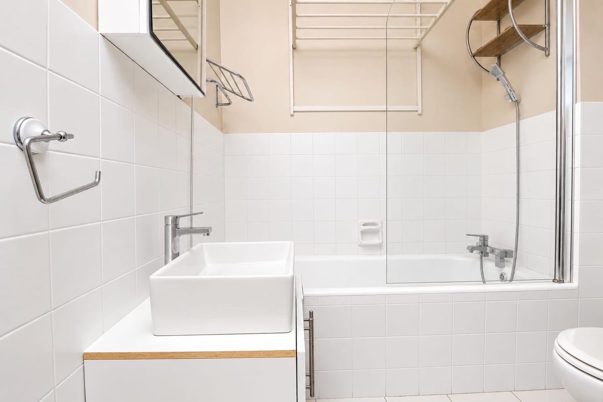 A clean, functional bathroom featuring a modern vessel sink, vanity cabinet, bathtub with a glass shower screen, and a wall-mounted medicine cabinet.