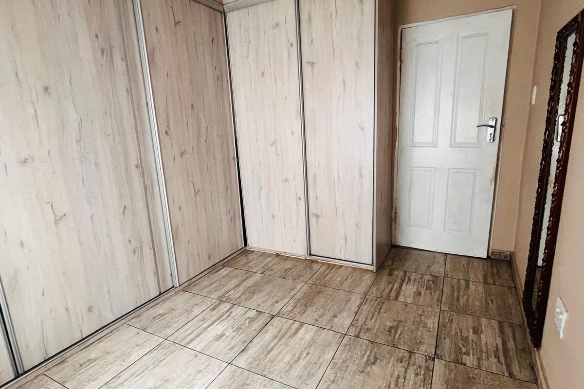 A clean bedroom space featuring light wood-grain built-in cupboards and matching tiled flooring, offering a neutral foundation for interior design.