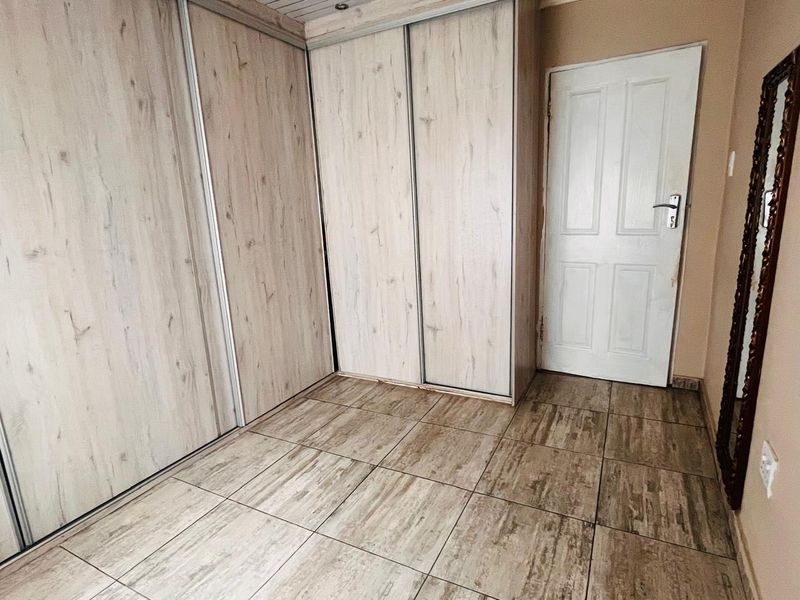 A clean bedroom space featuring light wood-grain built-in cupboards and matching tiled flooring, offering a neutral foundation for interior design.
