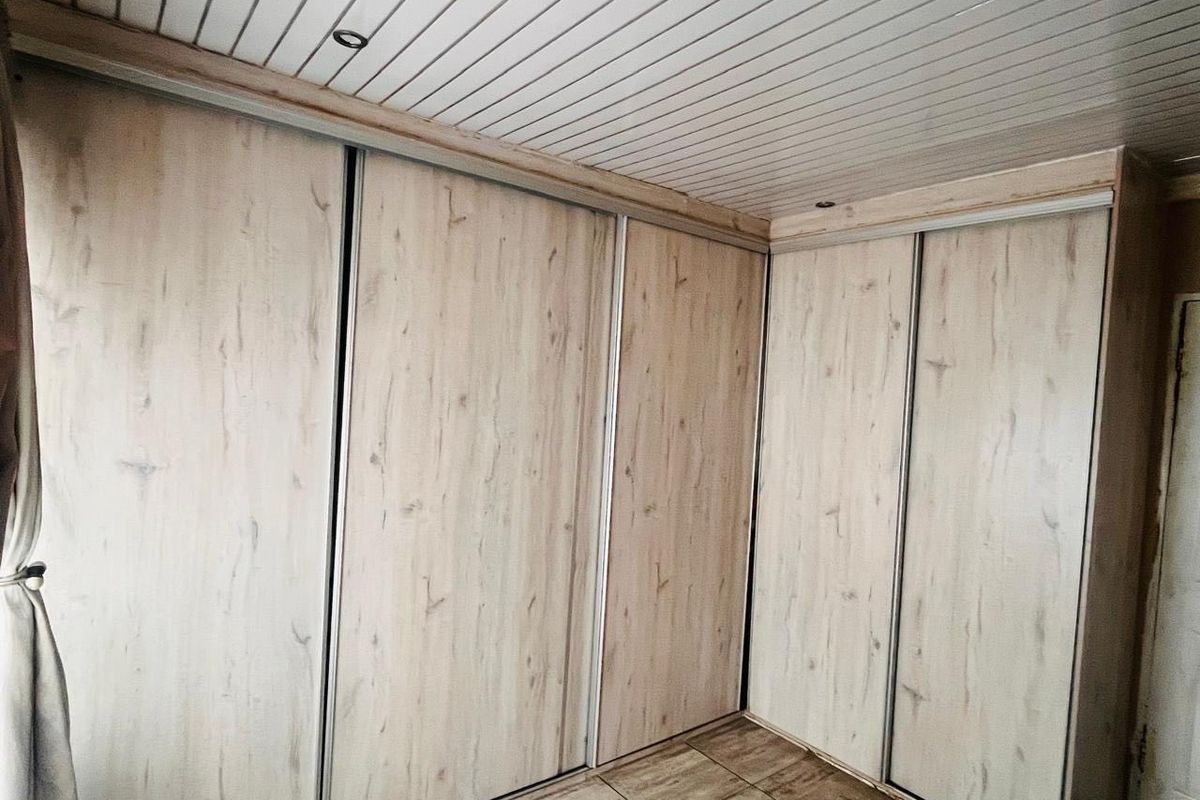 A bedroom featuring extensive built-in sliding door cupboards, tiled flooring, and a white tongue and groove ceiling with recessed lighting.