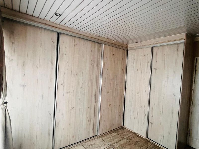 A bedroom featuring extensive built-in sliding door cupboards, tiled flooring, and a white tongue and groove ceiling with recessed lighting.