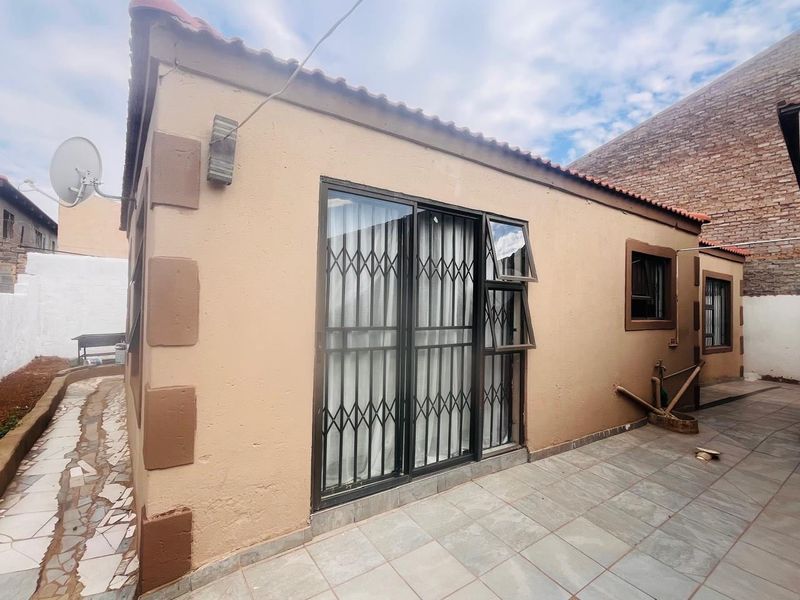 Rear exterior view of the property featuring a tiled patio area, sliding glass doors with security gates, and a tiled roof.