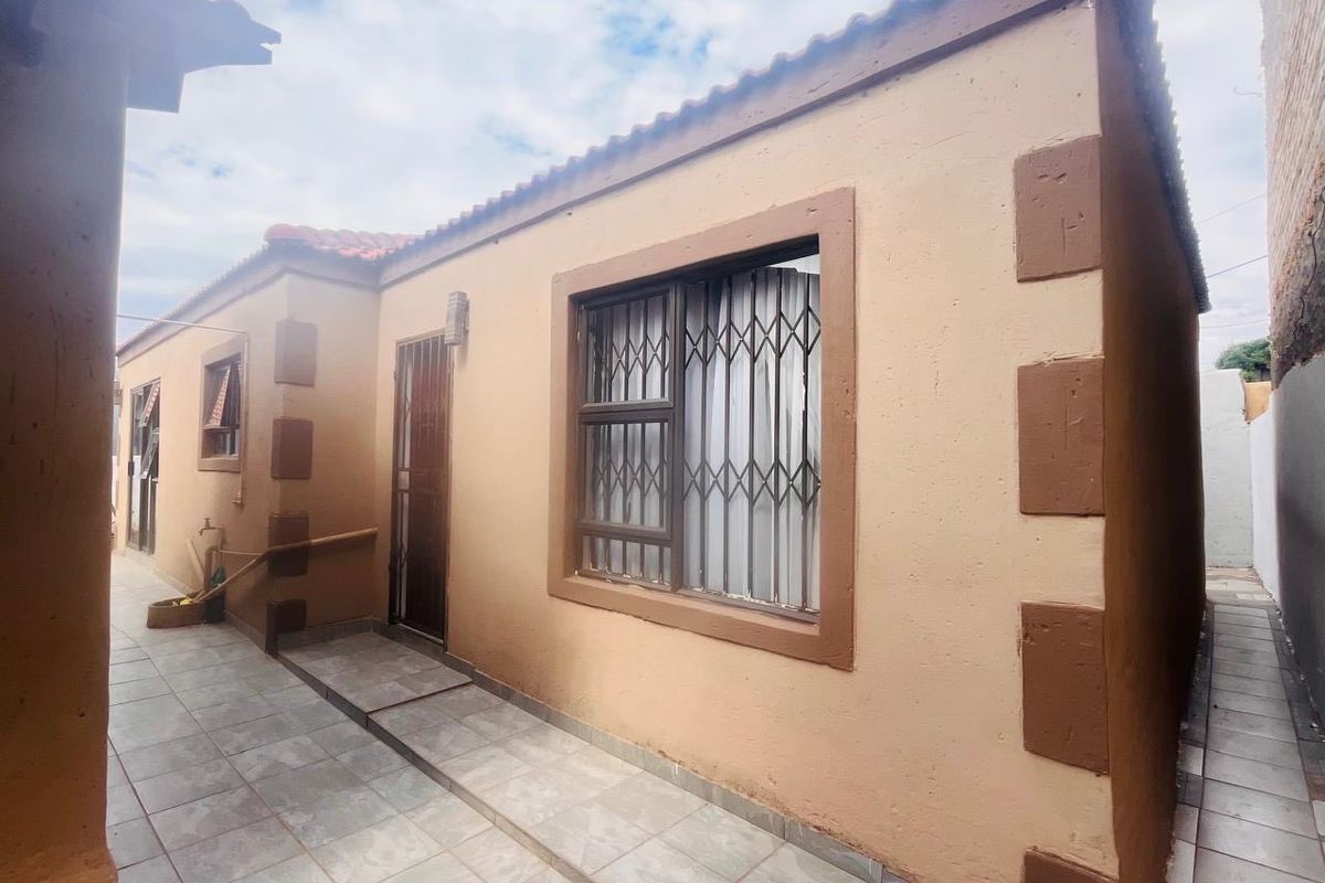 Rear exterior view of the property featuring tiled patio flooring, security bars on windows, and a secure entrance door.