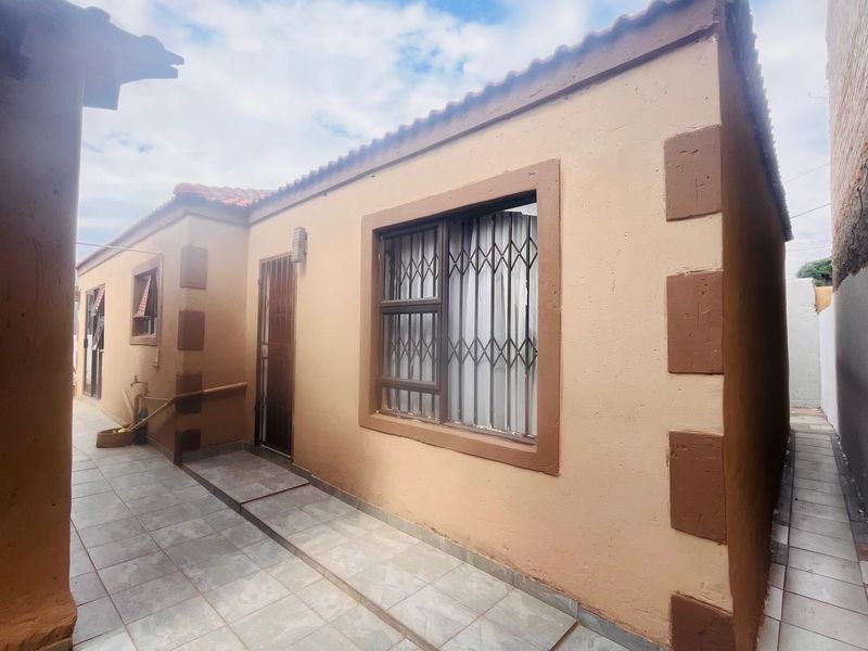 Rear exterior view of the property featuring tiled patio flooring, security bars on windows, and a secure entrance door.