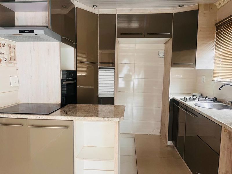 Modern kitchen featuring high-gloss cabinetry, stone countertops, integrated oven, extractor fan, and a stainless steel sink with tiled splashback.