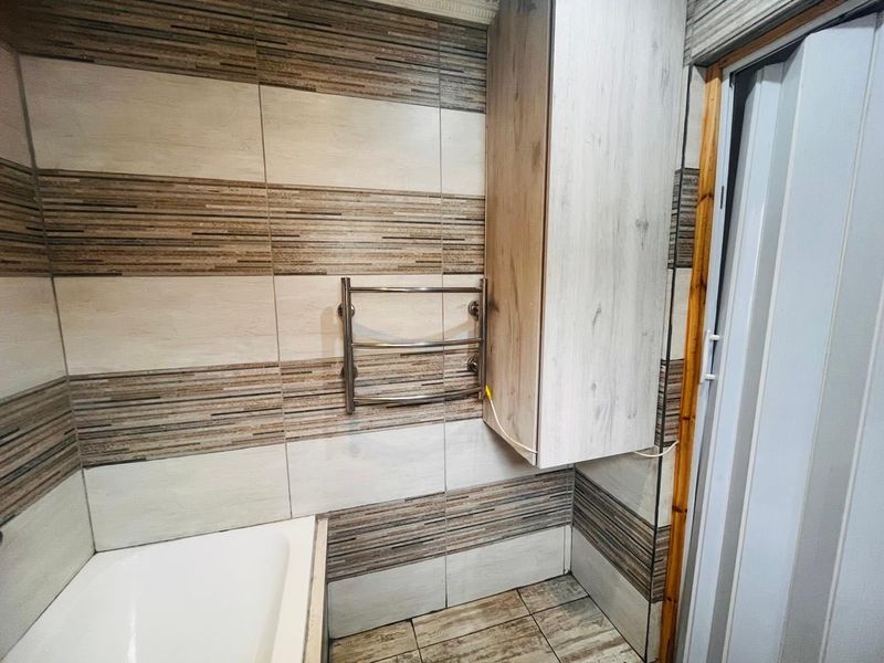 A bathroom featuring tiled walls and flooring, a built-in wall cabinet, and a heated towel rail, with a bathtub visible in the corner.