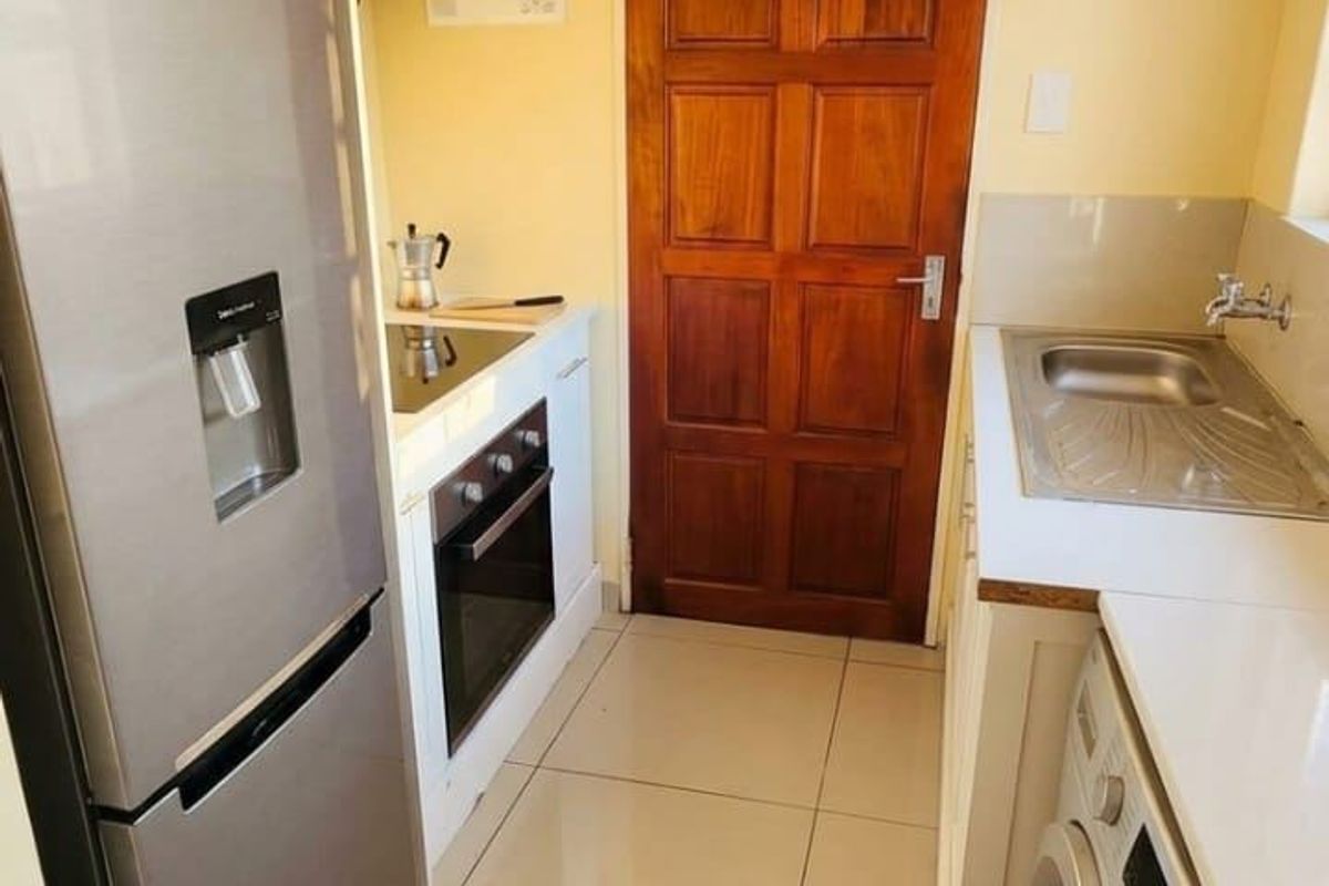 Compact kitchen featuring white cabinetry, stainless steel sink, built-in oven, hob, and tiled flooring, providing a functional and efficient workspace.
