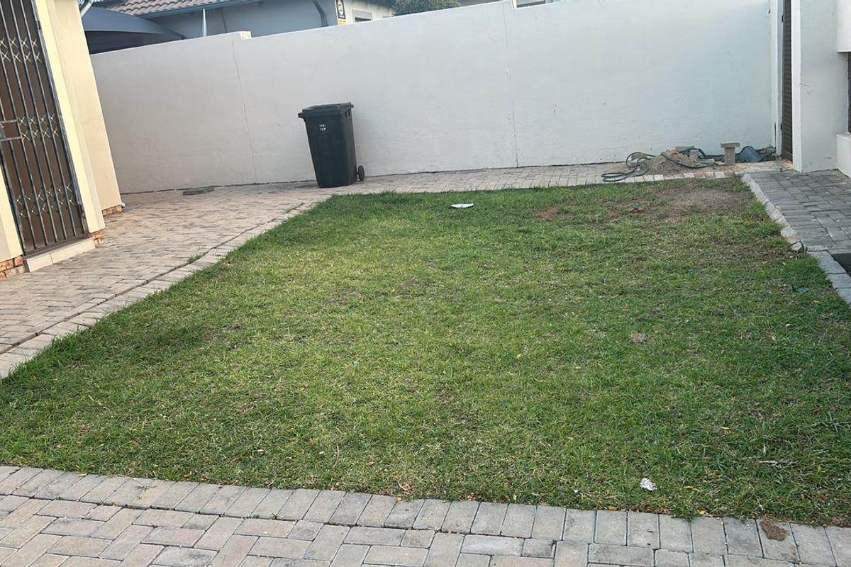 A compact rear garden featuring a small lawn area surrounded by paved pathways and a secure boundary wall.