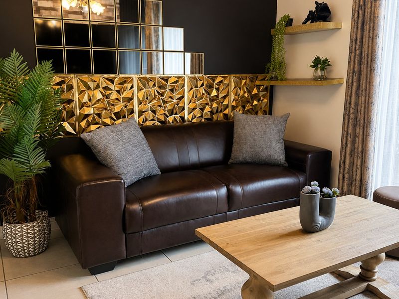 A well-maintained living room featuring a decorative gold-toned wall panel, mirrored accents, and neutral tiled flooring.