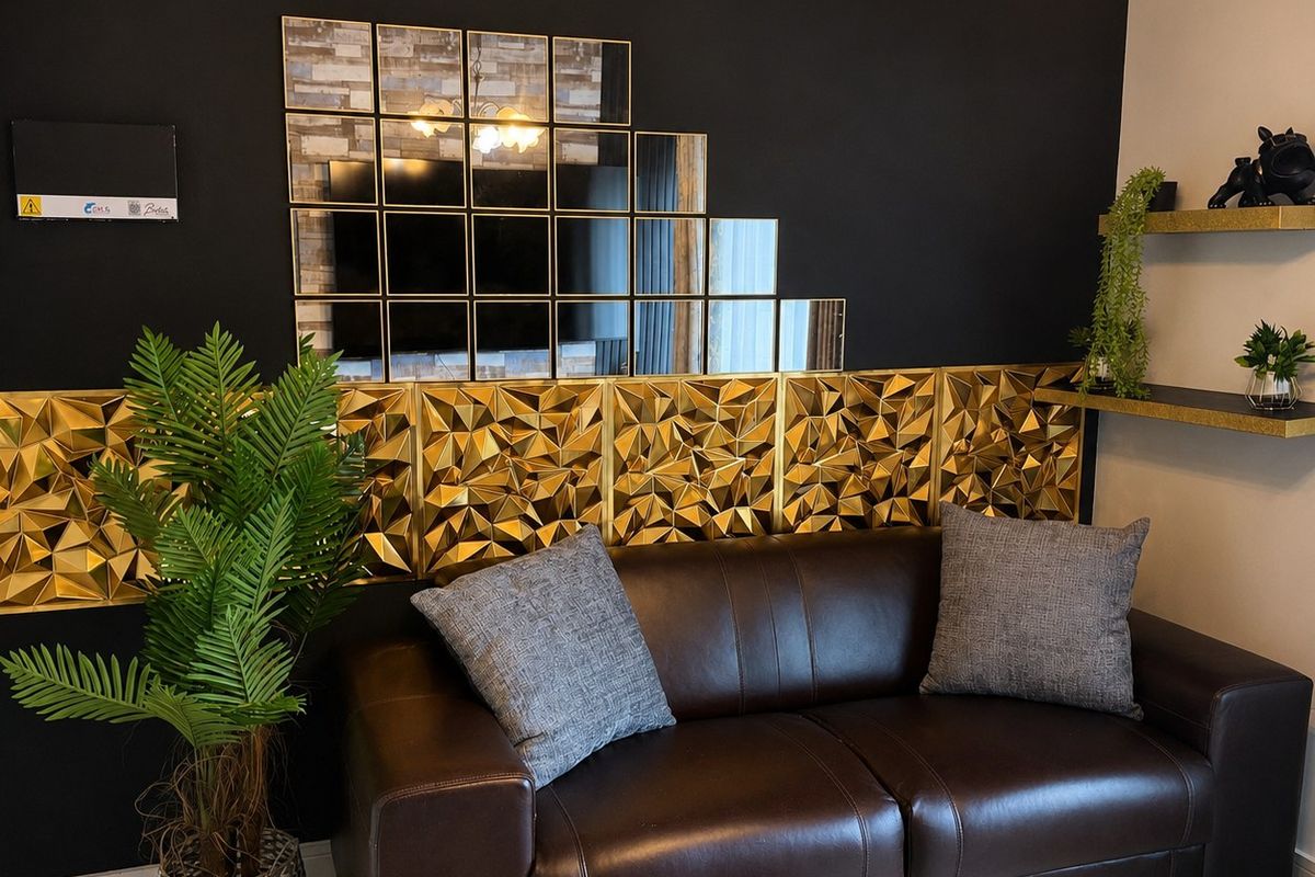 A living room area featuring dark accent walls, gold geometric wall paneling, tiled flooring, and built-in wall shelving.