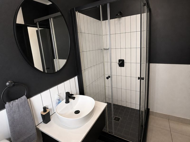 Modern bathroom featuring a sleek black and white color scheme, a glass-enclosed shower, a contemporary vessel sink vanity, and a circular wall mirror.