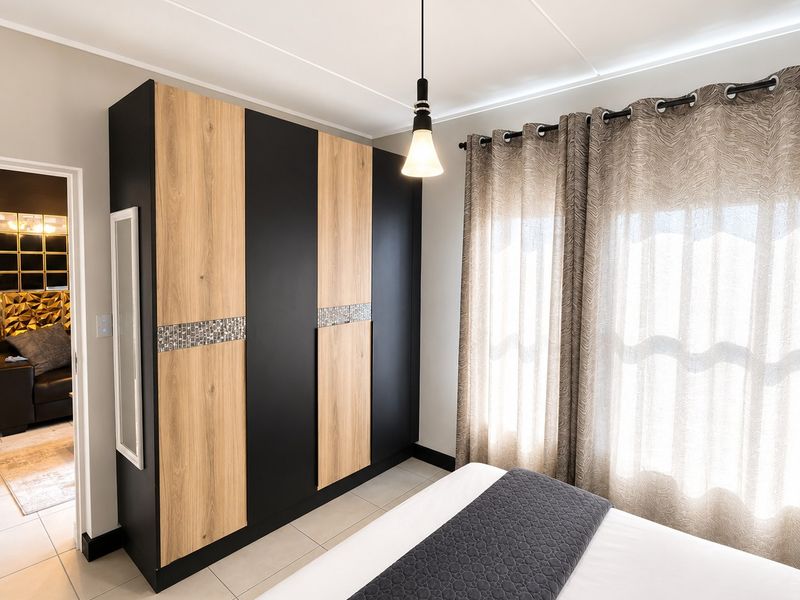 A well-maintained bedroom featuring modern built-in wardrobes with wood and black finishes, tiled flooring, and a contemporary pendant light fixture.