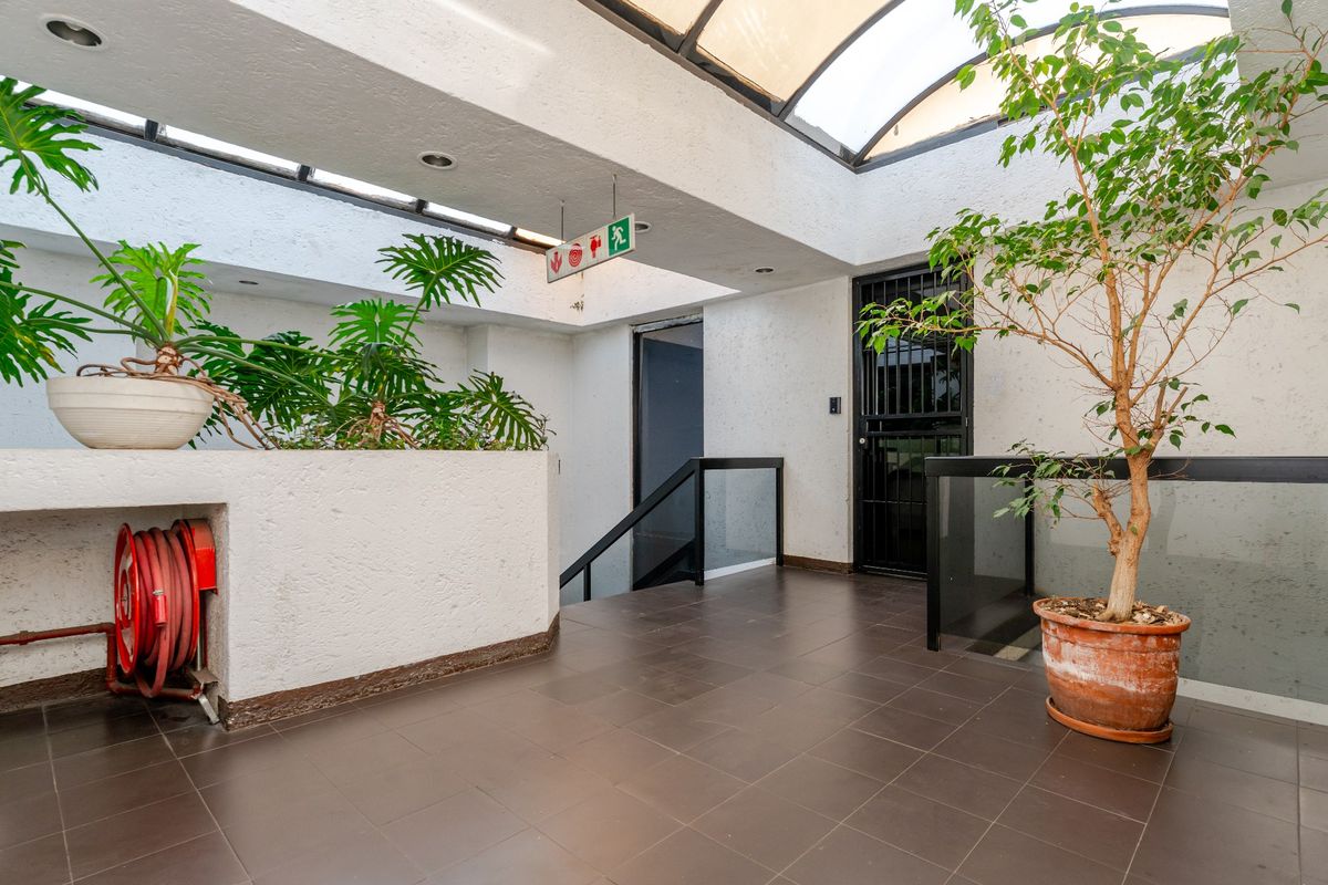 A bright commercial hallway featuring a large skylight, tiled flooring, a fire hose reel, and a secure entrance gate.