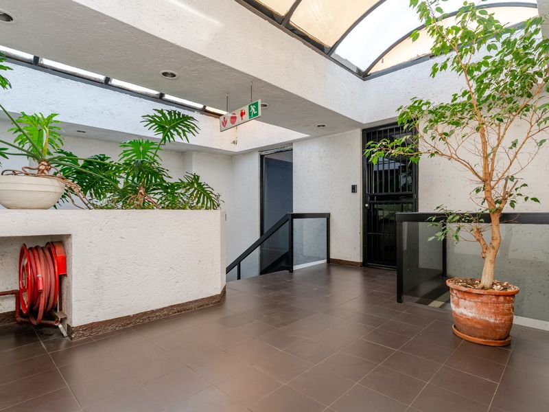 A bright commercial hallway featuring a large skylight, tiled flooring, a fire hose reel, and a secure entrance gate.