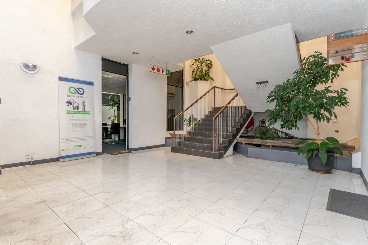 Spacious commercial building entrance lobby featuring tiled flooring, a central staircase with metal handrails, and integrated planter boxes.