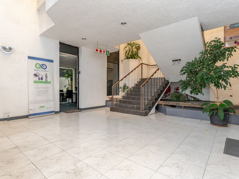 Spacious commercial building entrance lobby featuring tiled flooring, a central staircase with metal handrails, and integrated planter boxes.