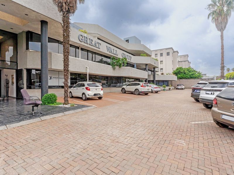Front exterior view of a commercial office building featuring a paved parking area, covered entrance, and prominent building signage.