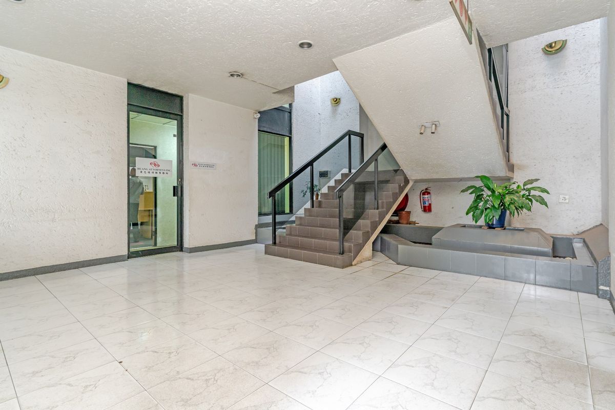 A spacious commercial building entrance lobby featuring tiled flooring, a central staircase, and glass-paneled office access.