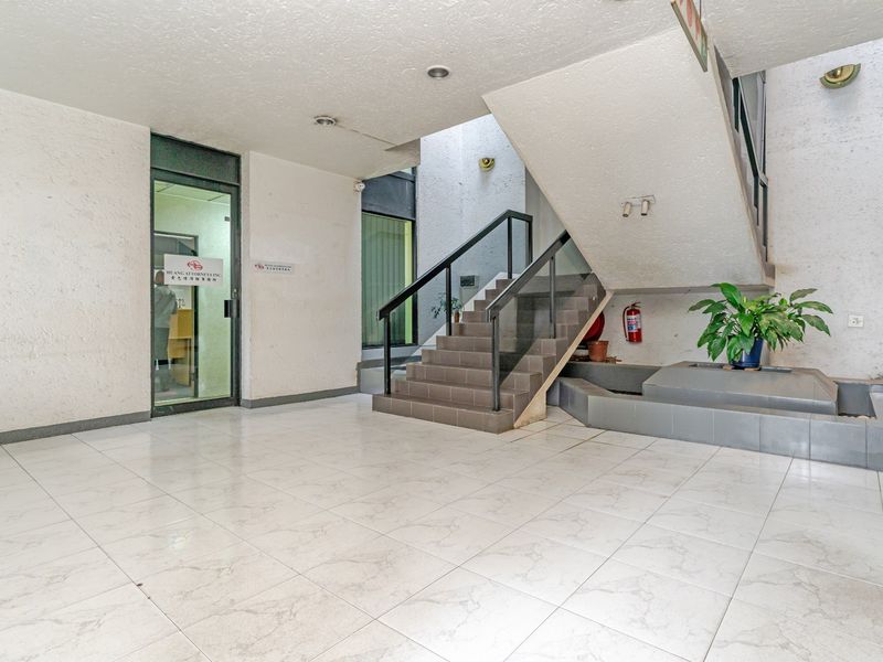 A spacious commercial building entrance lobby featuring tiled flooring, a central staircase, and glass-paneled office access.