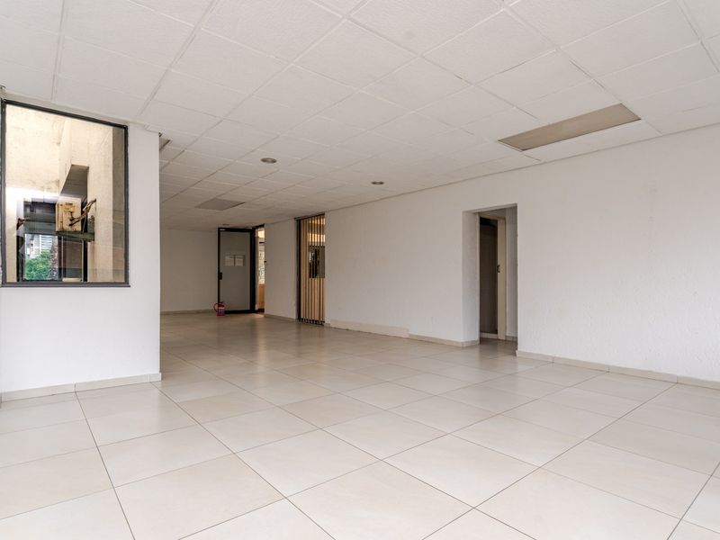An empty, open-plan commercial office space featuring tiled flooring, a suspended ceiling with recessed lighting, and an internal window.