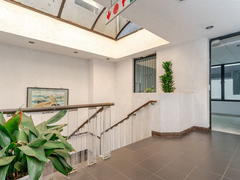 A commercial hallway featuring a staircase with a metal handrail, acrylic balustrade, and a large skylight providing natural light to the tiled space.