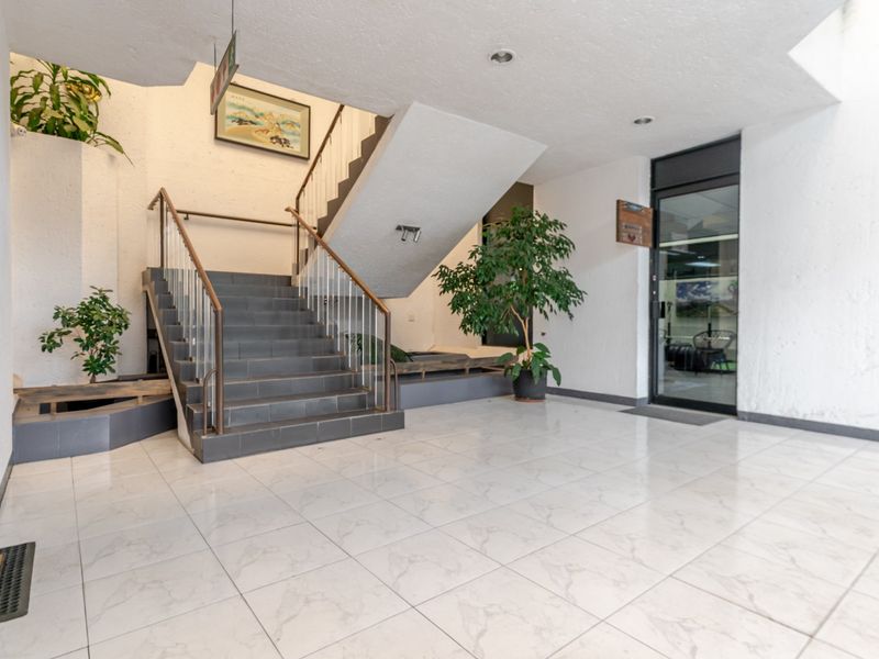 Spacious commercial building entrance lobby featuring tiled flooring, a central staircase with metal handrails, and a glass-paneled entrance door.