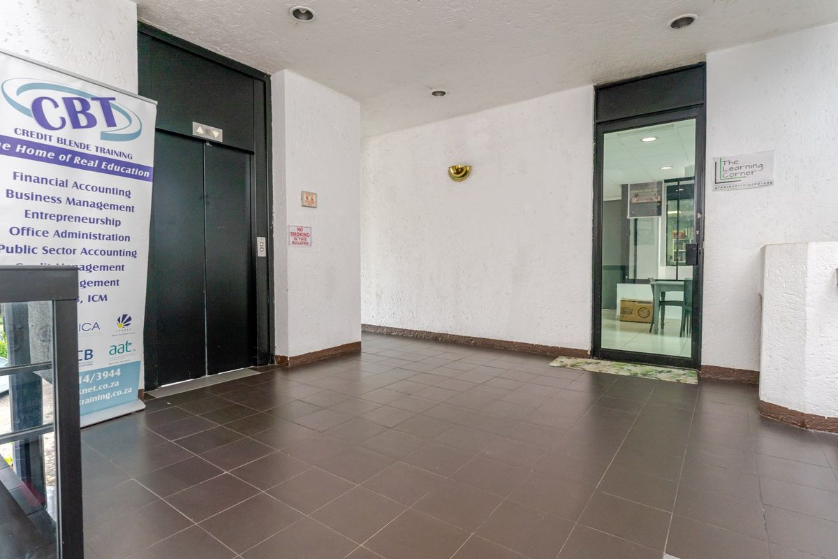 A commercial building entrance lobby featuring tiled flooring, a modern elevator, and a glass-paneled door leading into an office space.