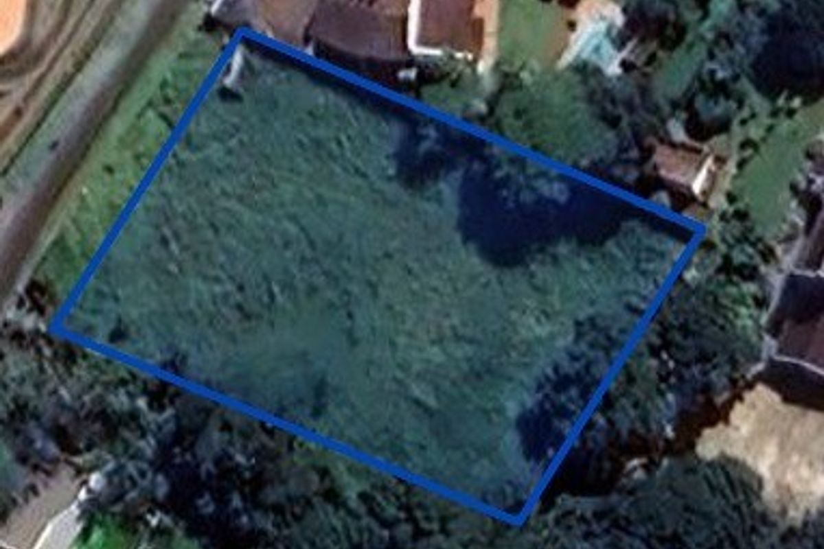 An aerial view of a vacant residential plot with a blue boundary outline indicating the property perimeter.