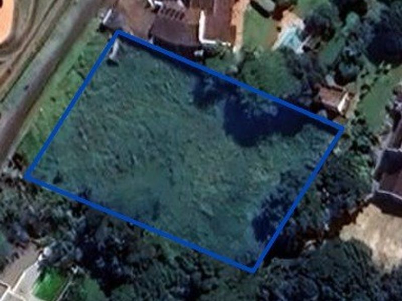 An aerial view of a vacant residential plot with a blue boundary outline indicating the property perimeter.