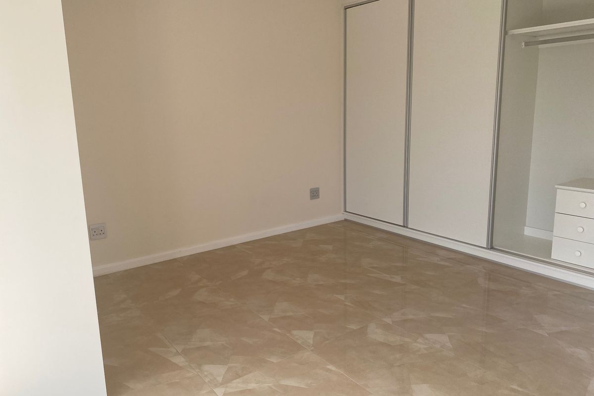 A clean, empty bedroom featuring neutral tiled flooring and a built-in wardrobe with sliding doors.