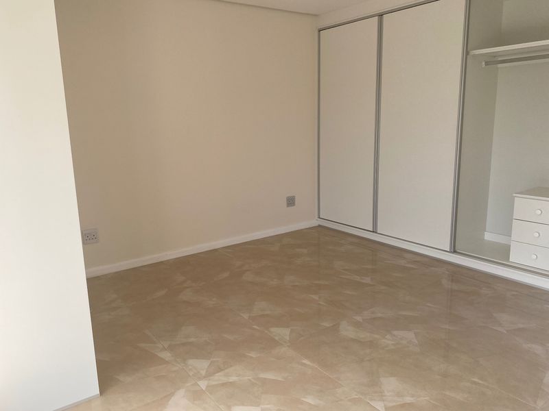 A clean, empty bedroom featuring neutral tiled flooring and a built-in wardrobe with sliding doors.