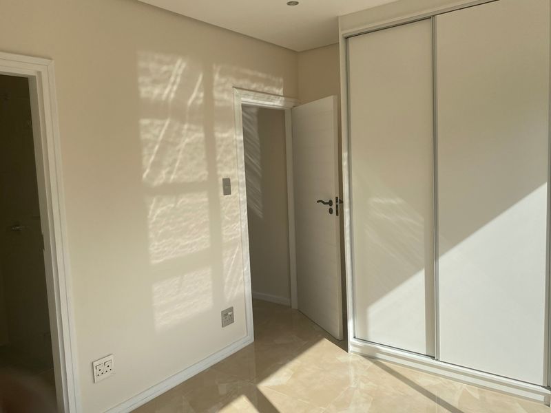 A bright, empty bedroom featuring neutral tiled flooring, built-in sliding door wardrobes, and clean finishes, ready for personalization.