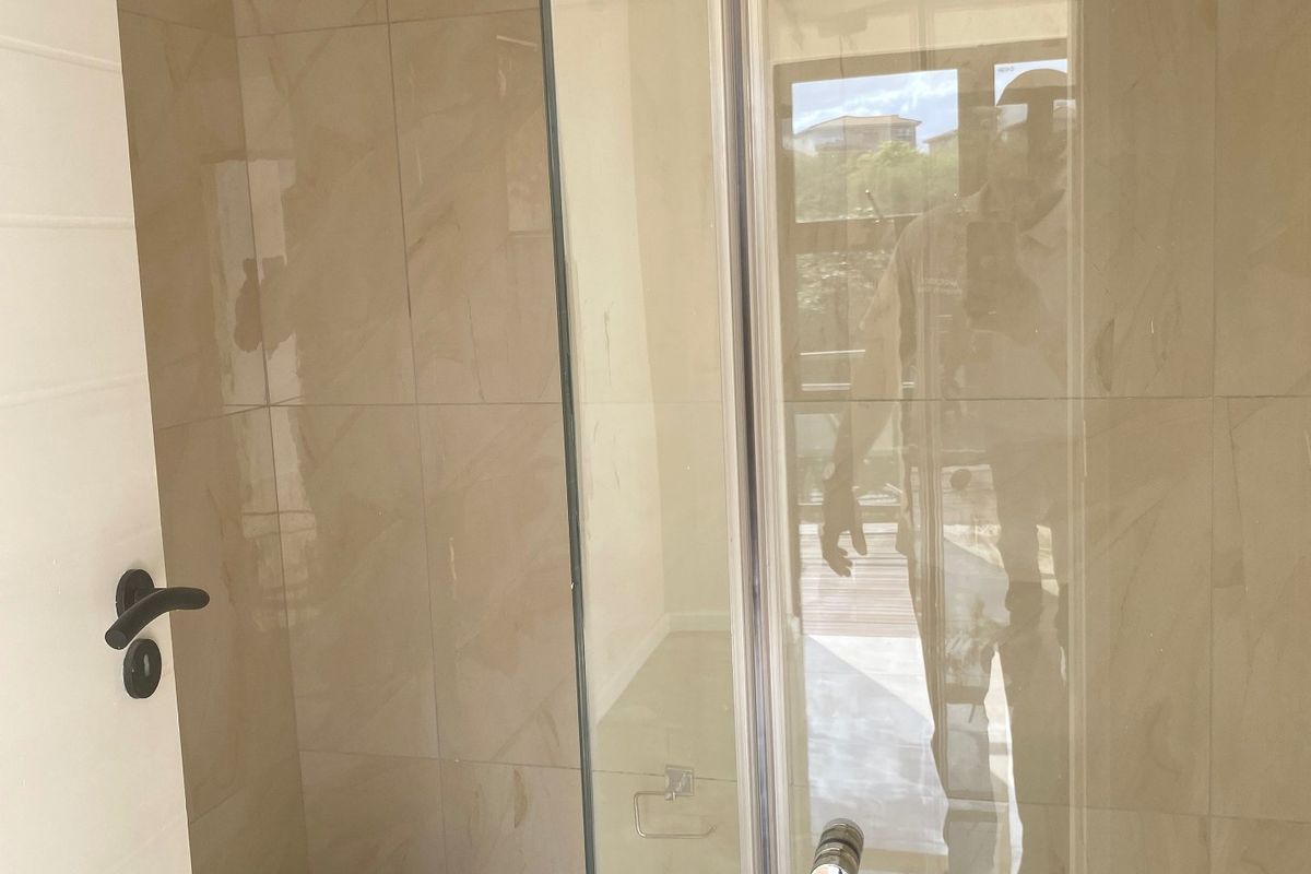 Modern bathroom featuring a glass-enclosed shower with a rain shower head and a wall-mounted toilet with neutral ceramic tiling.
