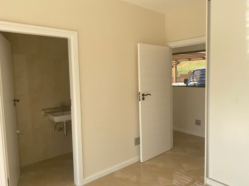 A clean, neutral hallway featuring tiled flooring, built-in storage, and access to an adjoining bathroom and secondary room.