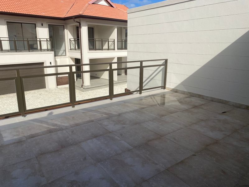 A spacious, tiled balcony featuring a modern glass and metal balustrade, offering an open outdoor area with views of the surrounding apartment complex.