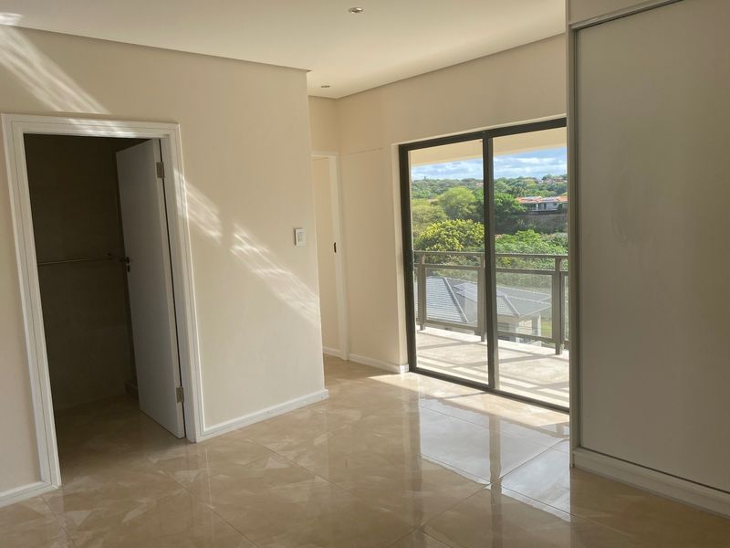 A bright, empty bedroom featuring tiled flooring, a built-in wardrobe, and sliding glass doors that open onto a balcony with scenic views.