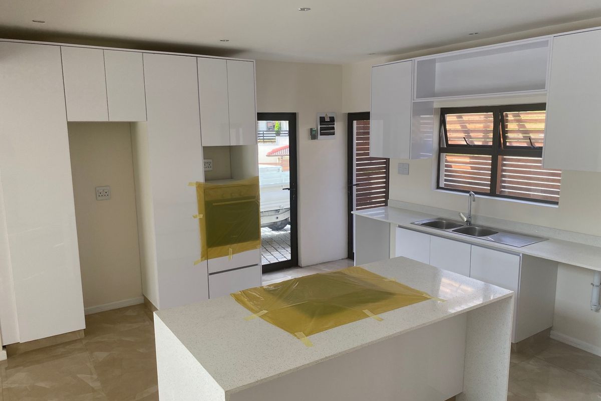 Modern kitchen featuring white cabinetry, stone countertops, a central island, and built-in oven, currently in the final stages of installation.