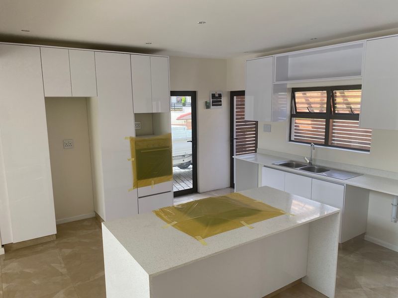 Modern kitchen featuring white cabinetry, stone countertops, a central island, and built-in oven, currently in the final stages of installation.