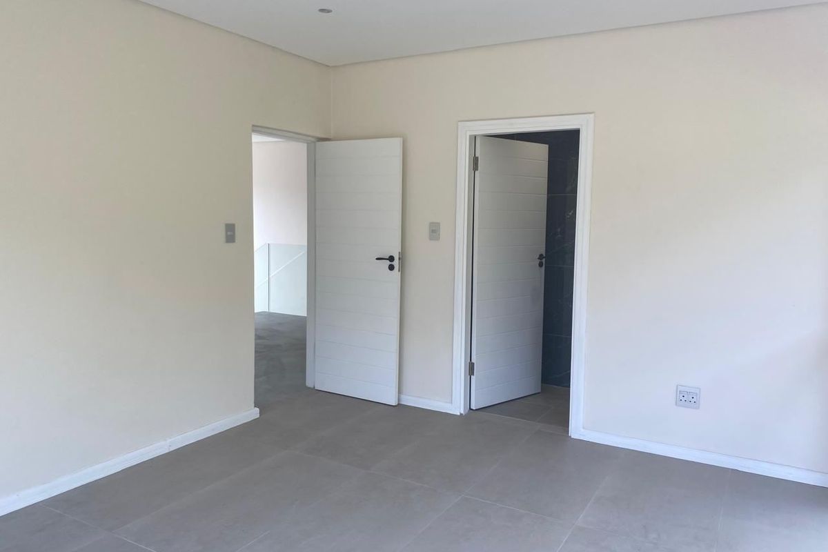 A clean, empty bedroom featuring neutral tiled flooring, recessed ceiling lighting, and two internal doors leading to adjacent spaces.
