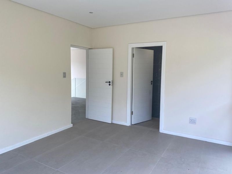 A clean, empty bedroom featuring neutral tiled flooring, recessed ceiling lighting, and two internal doors leading to adjacent spaces.