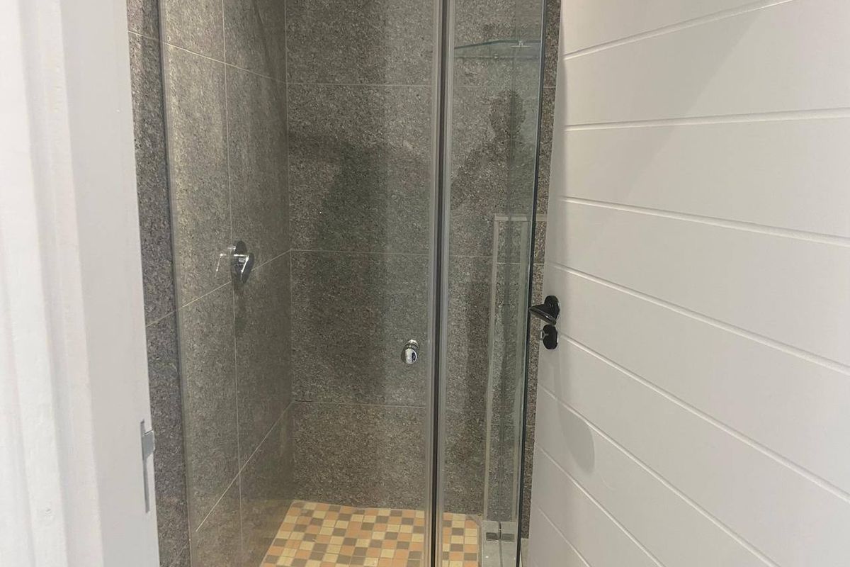 A clean, modern shower stall featuring grey stone-look wall tiles, mosaic floor tiling, and a glass enclosure, complemented by white shiplap wall paneling.